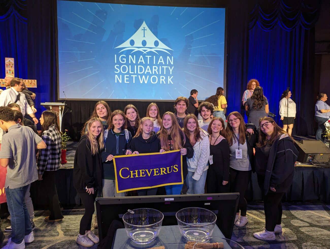 students smiling at Ignatian Family Teach-In holding school banner